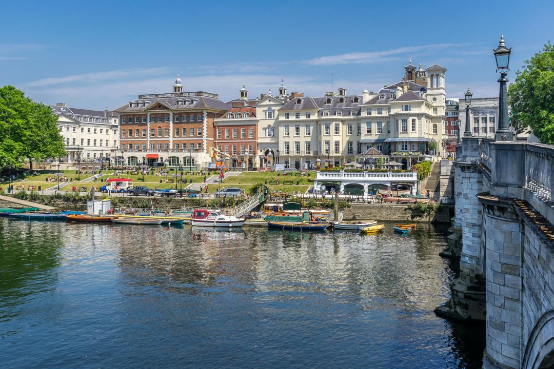 A group of boats sitting on top of a body of water in a small horbour with buildings in the background. 